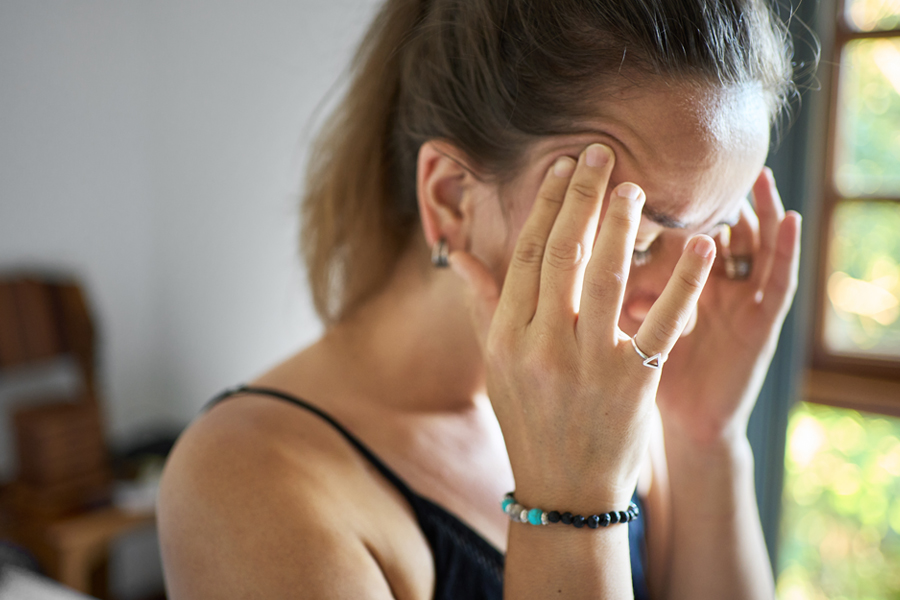 A woman holds her head while looking overwhelmed or not feeling well.