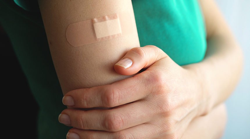 A young woman holds her hand, which is covered with a patch or adhesive bandage after vaccination or injection of medication.
