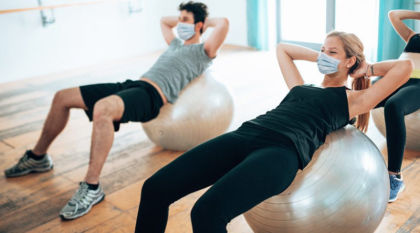 adults wearing masks work out in gym on exercise balls