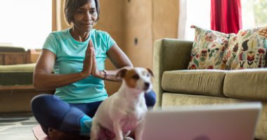 woman doing yoga with an on-line tutorial from her laptop during Covid Lockdown, dog looks on