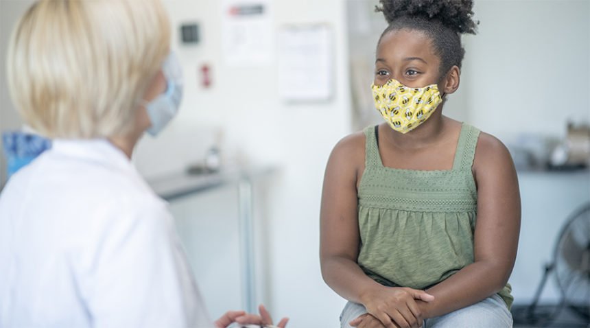 Teenage patient speaking with her paediatrician in a doctors office, both are wearing masks due to the new COVID-19 regulations and to avoid the transfer of germs.