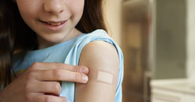 Girl showing her arm with a bandage after receiving the covid-19 vaccine.