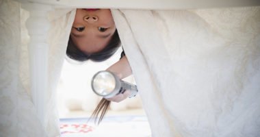 girl looking under bed with flashlight