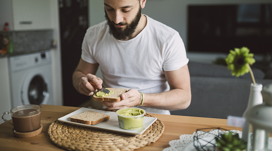 Young man having breakfast at home, toast with avocado cream