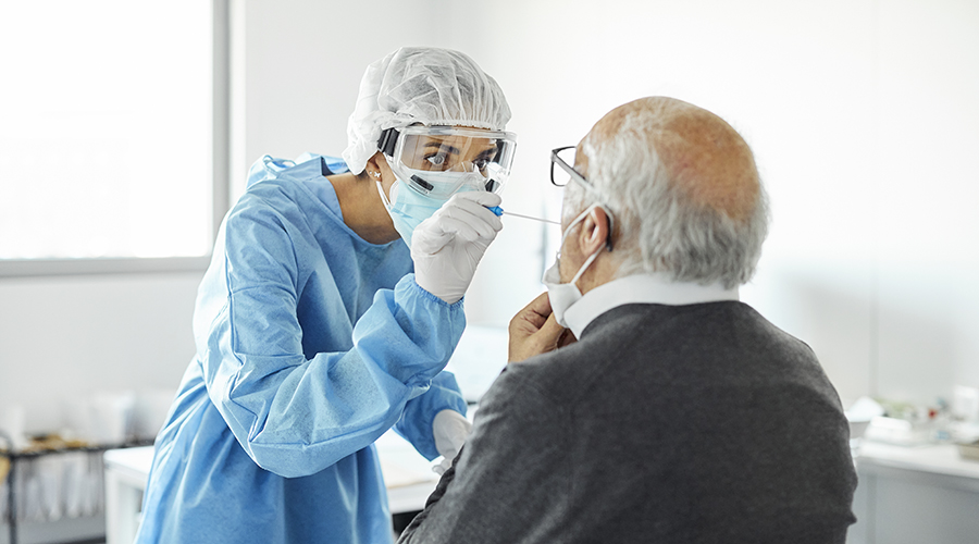 Doctor in protective suit taking sample for swab test of senior man. Medical professional is examining elderly patient during COVID-19 crisis