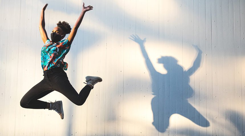 Woman, wearing mask, jumping in the air against a wall with her shadow