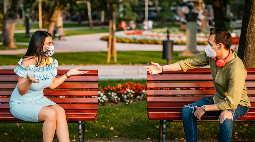 Young couple arguing in park , wearing masks and sitting on two different benches