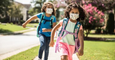 young girls wearing masks, backpacks as they walk to school