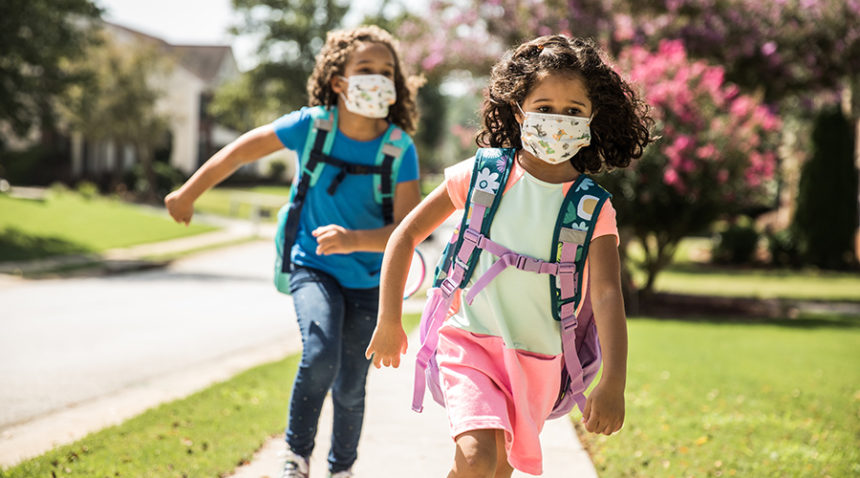 young girls wearing masks, backpacks as they walk to school