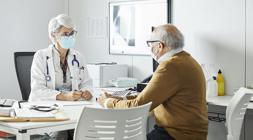 Doctor discussing with senior man, both wearing masks
