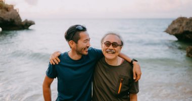 Senior father and adult son having a good time on beach at sunset