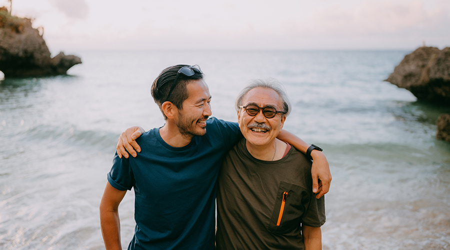 Senior father and adult son having a good time on beach at sunset