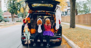 Children celebrating Halloween in trunk of car. Boy and girl with red pumpkins