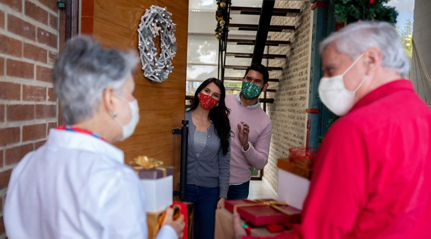 Happy senior couple arriving at their adult children's home for Christmas wearing facemasks and carrying presents