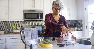 older woman makes a healthy smoothie in her kitchen