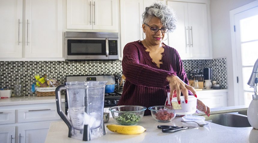 older woman makes a healthy smoothie in her kitchen