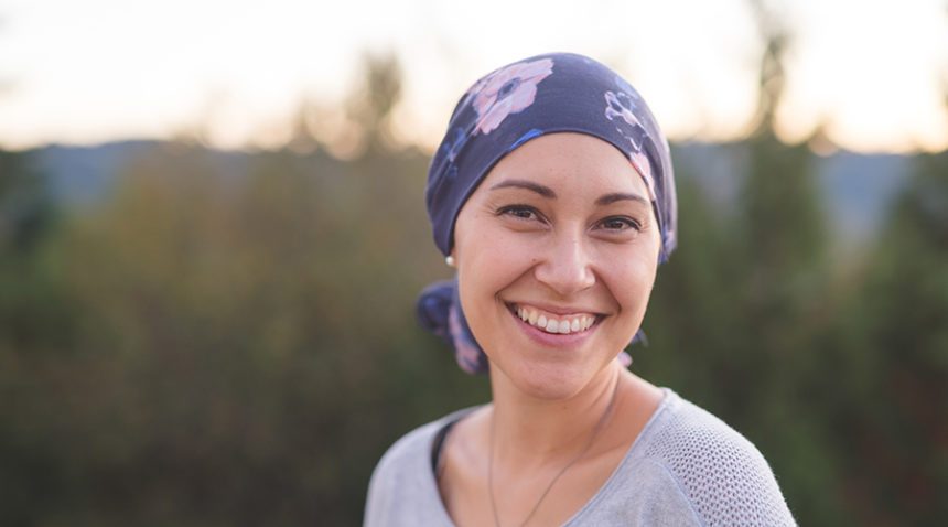 A beautiful young woman wearing a head wrap looks toward the camera and smiles radiantly