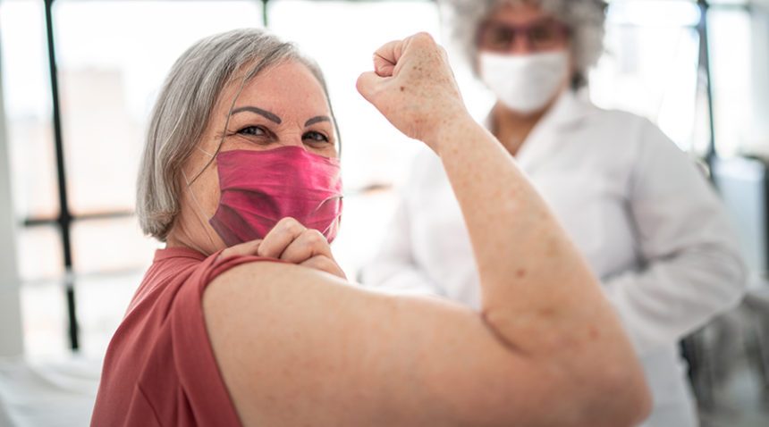 Older woman being vaccinated and flexing biceps muscle - wearing face mask