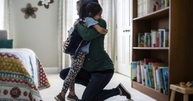 Mother embracing young daughter in bedroom before leaving for school