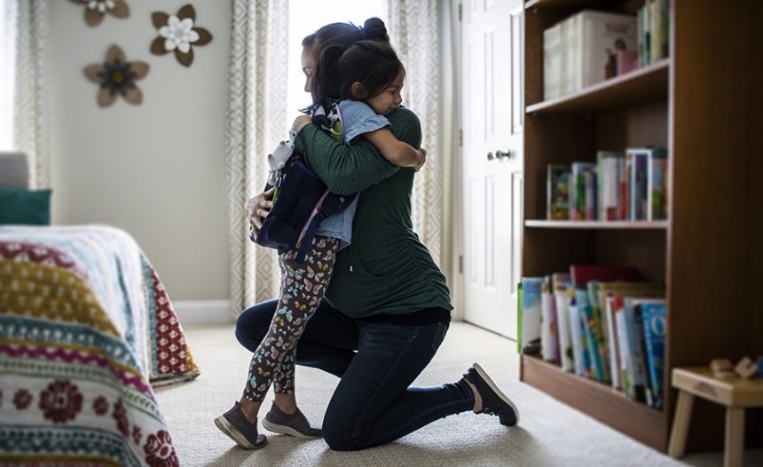 Mother embracing young daughter in bedroom before leaving for school