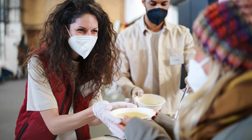 Volunteers serving food in soup kitchen, wearing masks
