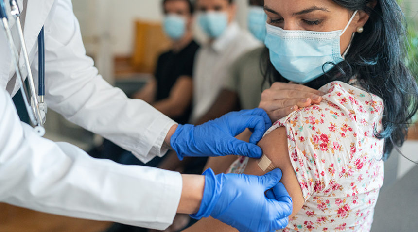 Doctor or nurse putting on bandage after Injecting COVID-19 vaccine into patient's arm in vaccination center