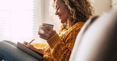 Happy woman at home, writes notes on a diary while drinking a cup of tea