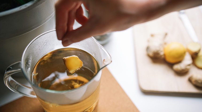 Cropped Hand Of Woman Adding Ginger Slice To Tea