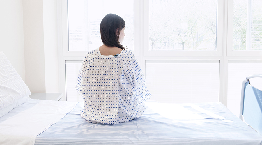 Teenage patient sitting on hospital bed, rear view.