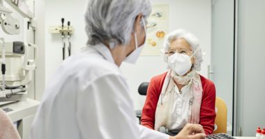 Doctor discussing with senior woman, both wearing KN95 masks.