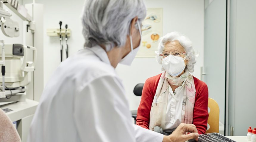 Doctor discussing with senior woman, both wearing KN95 masks.