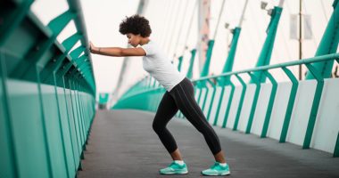 An athletic woman warming up before she starts to run on city bridge