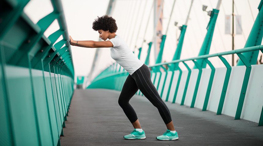 An athletic woman warming up before she starts to run on city bridge