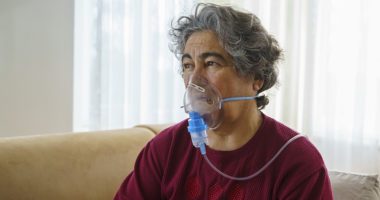 Senior woman inhaling through oxygen mask at home