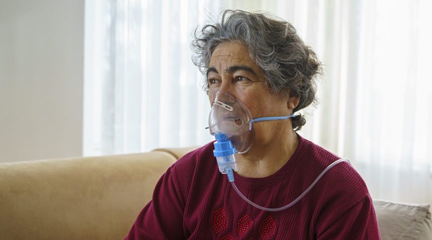 Senior woman inhaling through oxygen mask at home