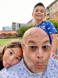 UNC Health colon cancer patient Greg Meddlin with his two kids outside on a park lawn