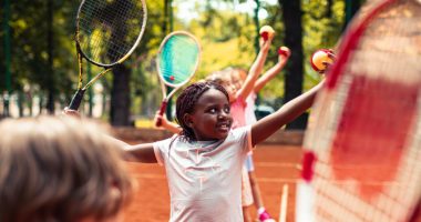 Close up of a group of kids on a tennis court learning how to serve a tennis ball