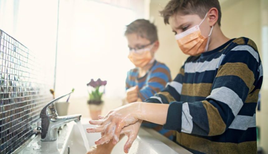 Two boys wearing face masks stand at sink while washing hands