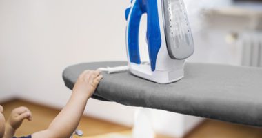 a small child reaches for the cord of an iron sitting on top of an ironing board