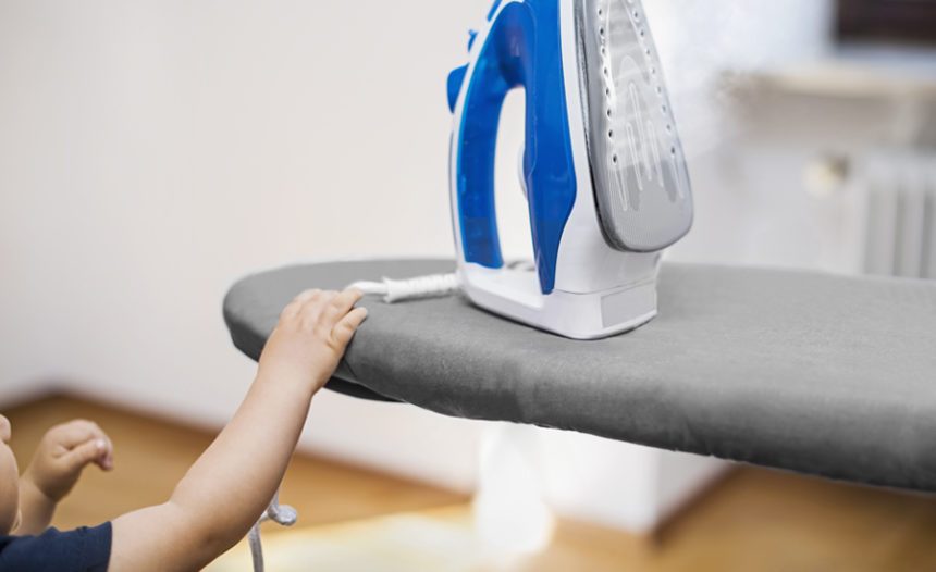 a small child reaches for the cord of an iron sitting on top of an ironing board