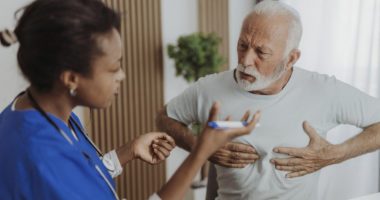 Older man clutches chest while talking to a provider