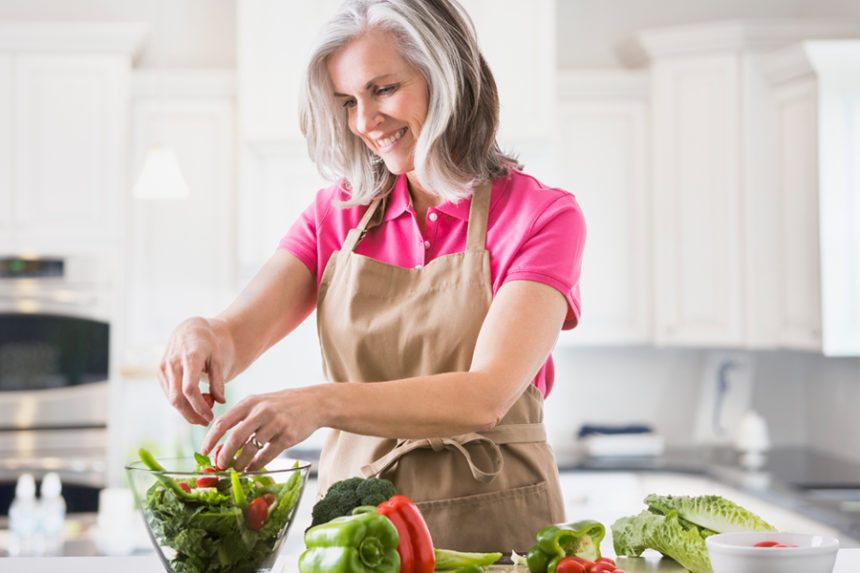 Fit older woman with gray hair makes a salad in a sleek, natural-light-filled kitchen