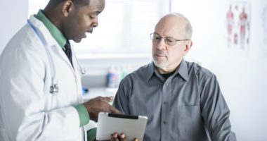 Male doctor talks to male patient, using a clipboard as a demonstrative