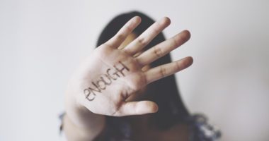 a woman holds up her palm to the camera, the word "enough" written in marker on her hand