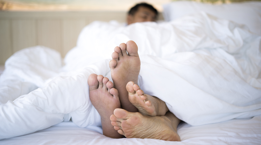 close-up view of two pairs of feet on a bed, sticking out from under the sheets.