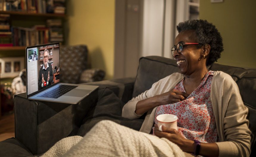 Woman sits on couch, laughing, while talking to therapist on a laptop over a virtual call