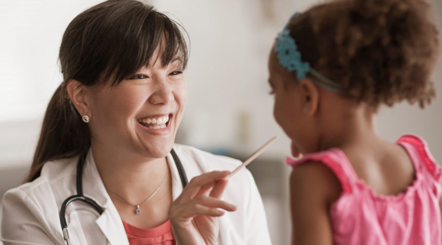 Provider smiles as she holds a swab toward a child patient's mouth