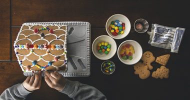 overhead shot of a child decorating a gingerbread house with candies