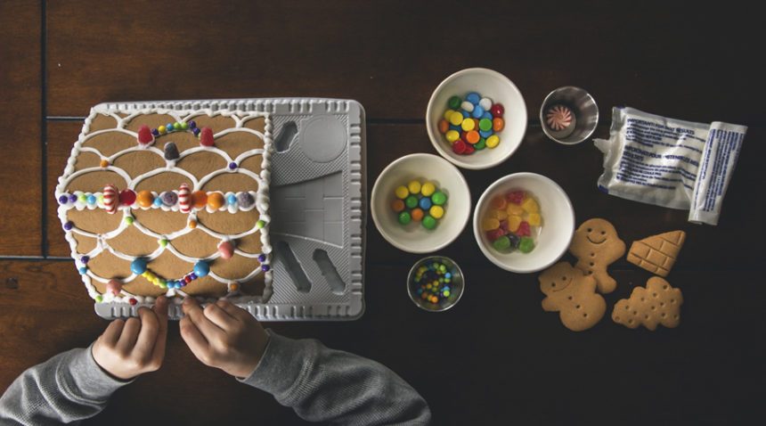 overhead shot of a child decorating a gingerbread house with candies