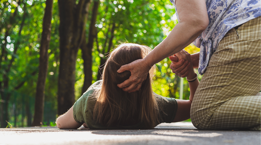 adult puts hand behind the head of a child that has fallen down outside